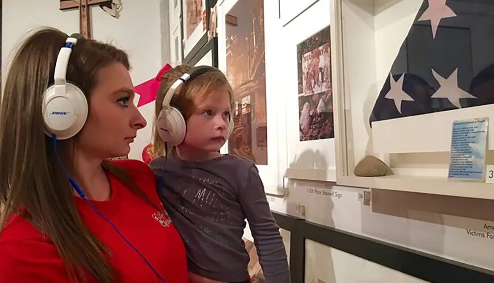 A woman and a child are intently looking at an exhibition while wearing headphones possibly listening to an audio guide