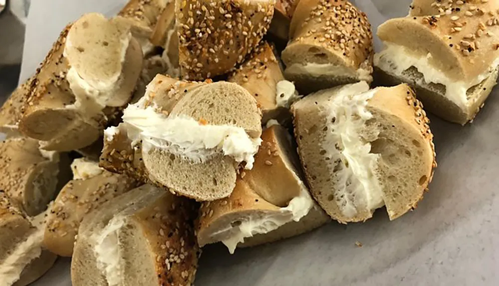 The image shows multiple slices of bagel generously smeared with cream cheese some sprinkled with sesame seeds