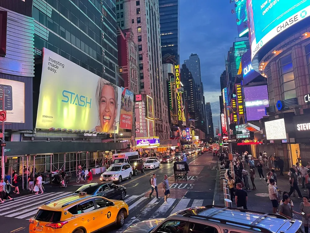 The image shows a bustling Times Square in the evening with vibrant billboards busy traffic and crowds of pedestrians