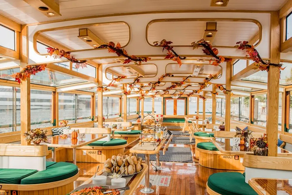 The image shows a warmly lit wood-paneled interior of a boat or ship elegantly arranged for dining with tables set with bread rolls floral decorations and autumn-themed garlands