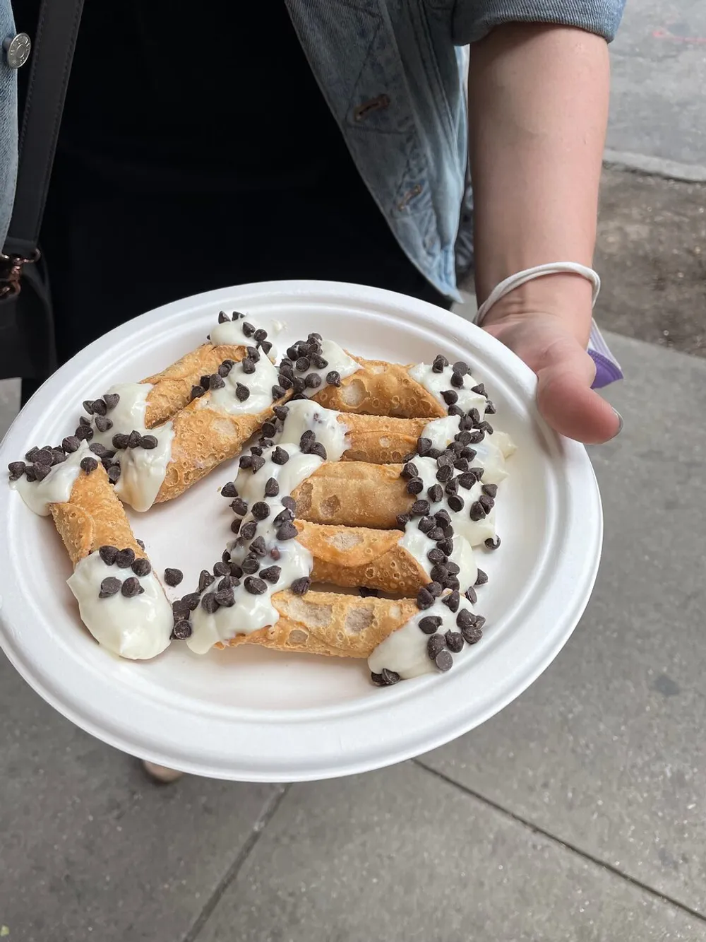 A person is holding a plate of four cannoli topped with cream and sprinkled with chocolate chips