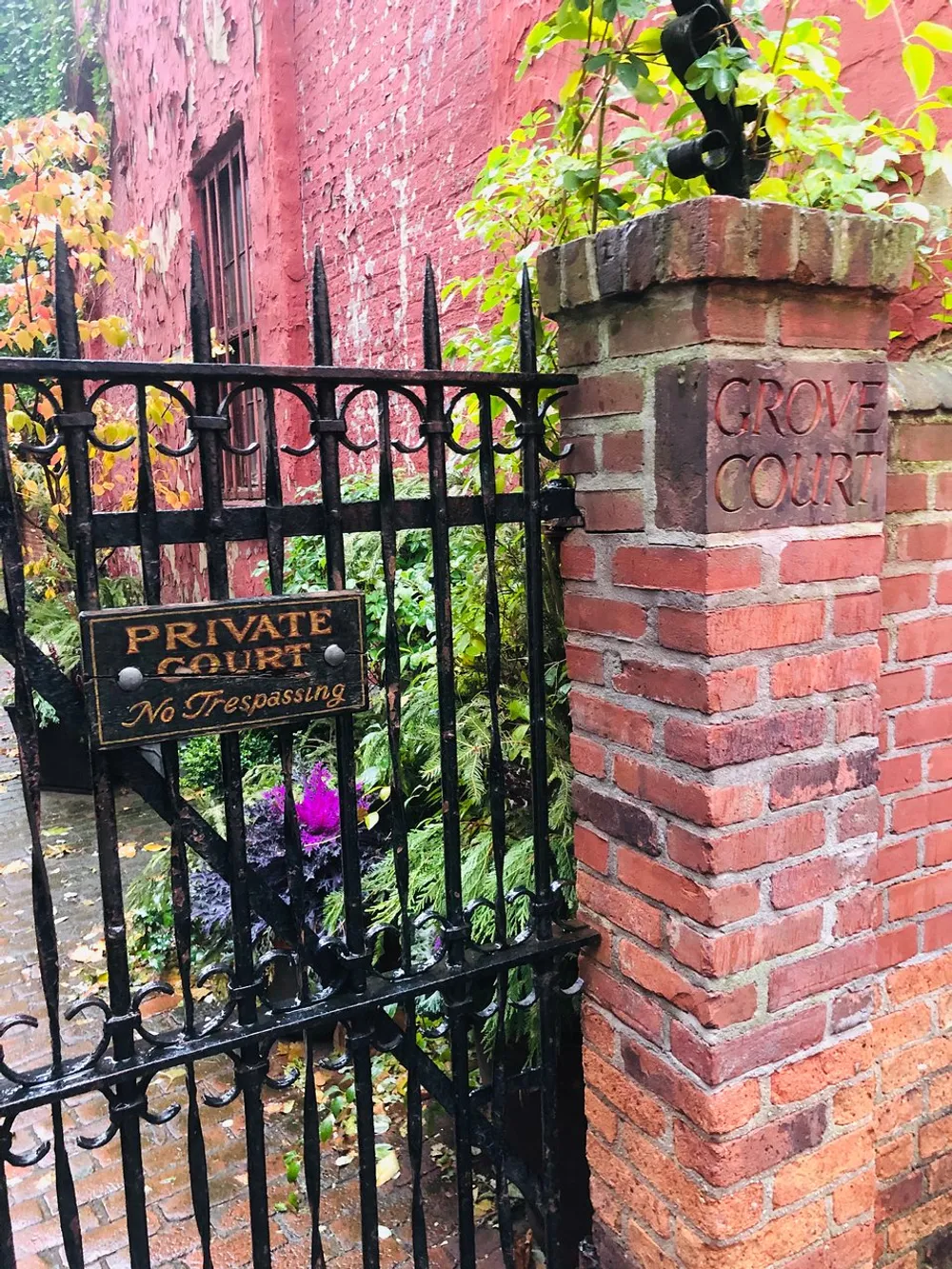 The image shows a weathered brick pillar with the engraved words GROVE COURT next to a black wrought iron gate that bears a sign reading PRIVATE COURT No Trespassing leading to a garden behind it