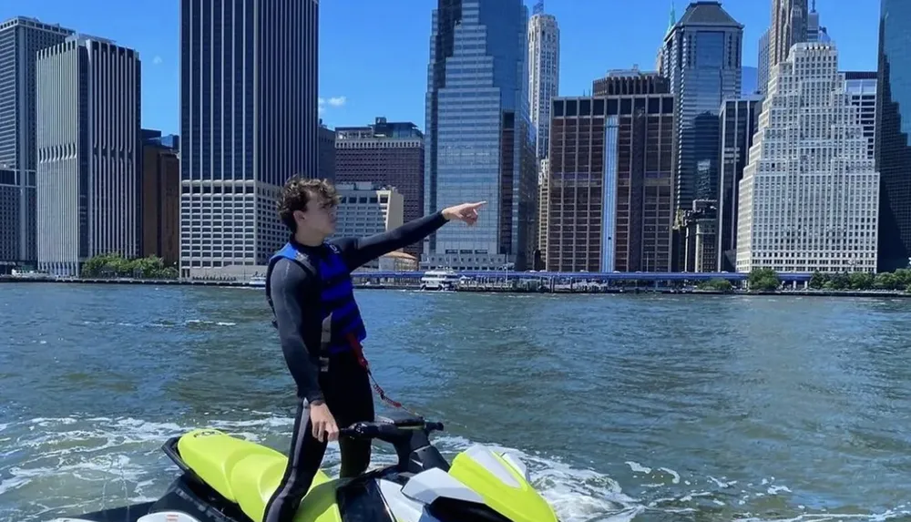 A person is standing on a jet ski pointing towards the skyline of a city across the water