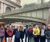 A diverse group of people are posing for a photo in front of the Grand Central Terminal entrance at Pershing Square Plaza