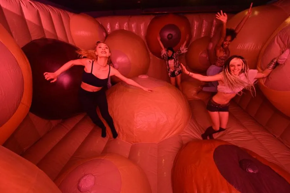 Several people are joyfully interacting with oversized bouncy ball-like structures in a red-lit inflatable playground