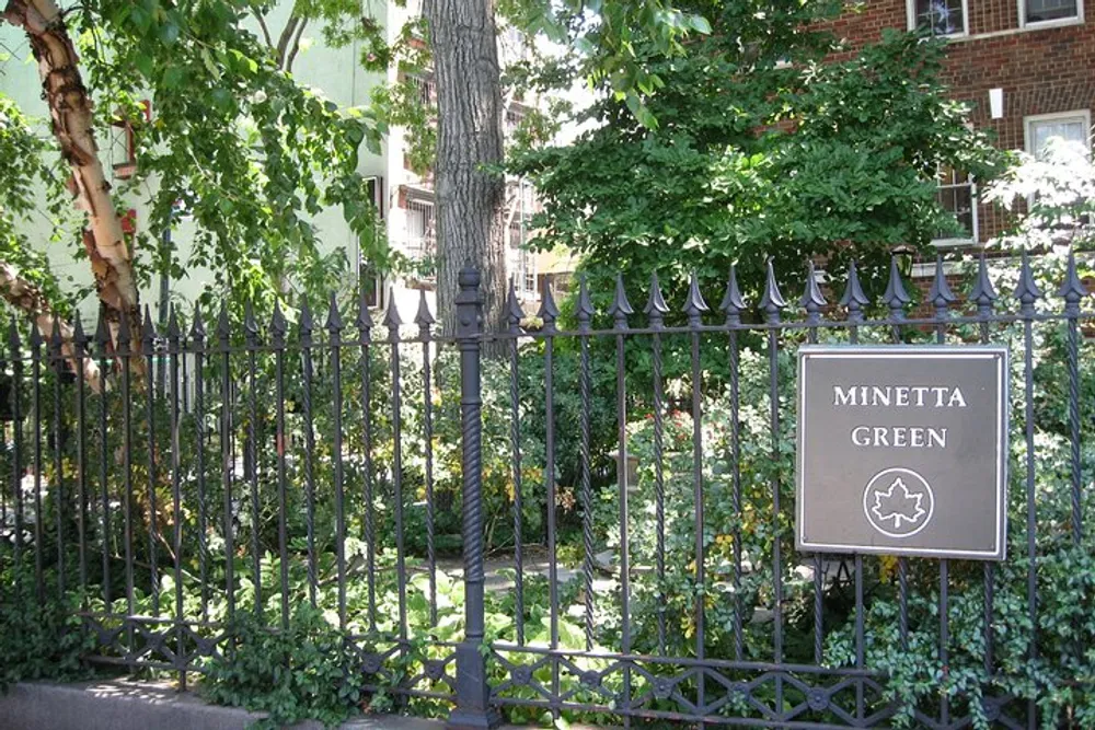 The image shows a lush green space behind a black iron fence with a sign that says Minetta Green