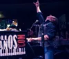 A passionate performer is raising his index finger to the sky while singing into a microphone at a lively piano bar with an audience enjoying the show in the background