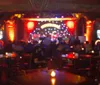 A passionate performer is raising his index finger to the sky while singing into a microphone at a lively piano bar with an audience enjoying the show in the background