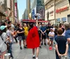 A performer wearing a red cloak is engaging with a crowd of onlookers in a bustling Times Square