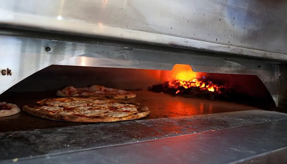 Pizzas are cooking inside a wood-fired oven with a visible flame at the back