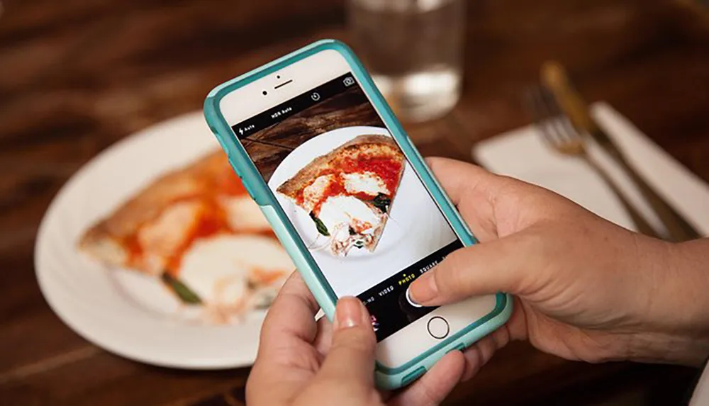 A person is photographing a slice of pizza on a plate using a smartphone