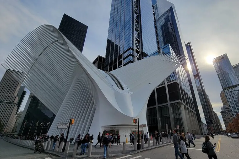 This image shows pedestrians near the distinctive wing-like architecture of the Oculus in New York City set against a backdrop of skyscrapers under a partly cloudy sky