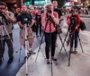 A group of photographers with their cameras mounted on tripods are taking pictures in a bustling urban setting at night