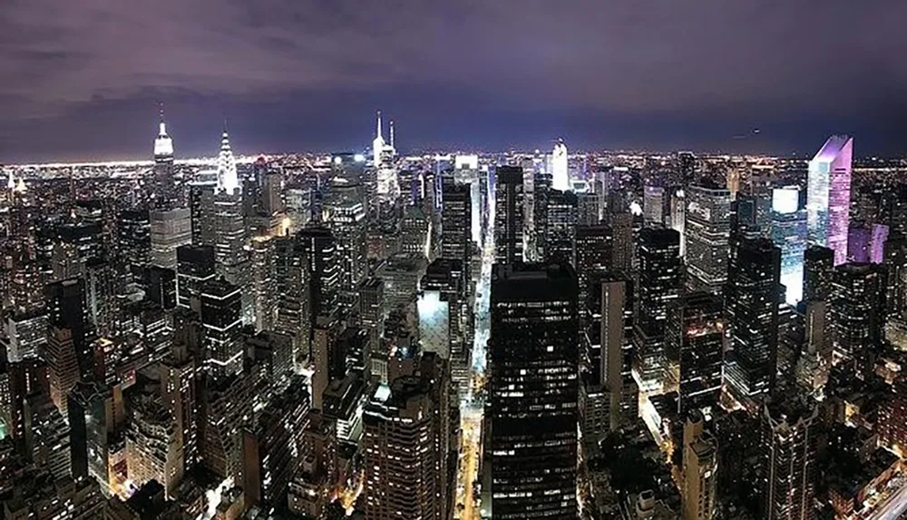 A nighttime panorama showcases the illuminated skyscrapers of a densely packed urban skyline