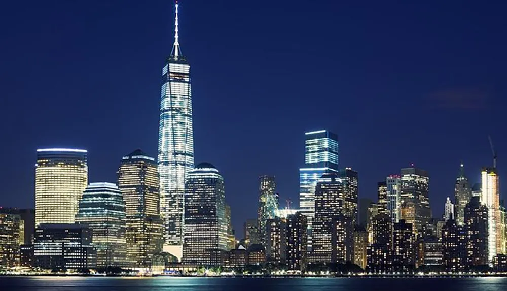 The image displays a night view of a lit-up skyline featuring several skyscrapers including a prominently illuminated tall tower reflecting the urban cityscapes vibrant atmosphere