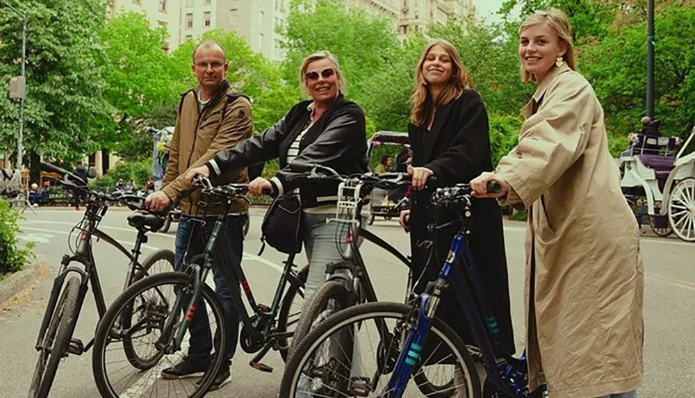 Four people are happily posing with bicycles on a tree-lined urban street