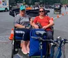 Two people are smiling for a photo while sitting in a pedicab on a city street