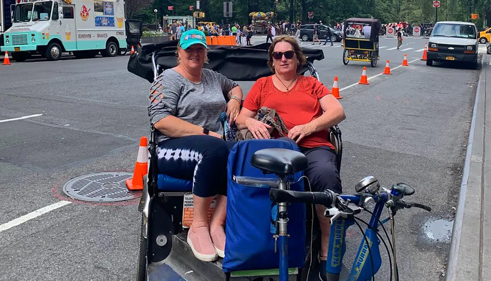 Two people are smiling for a photo while sitting in a pedicab on a city street