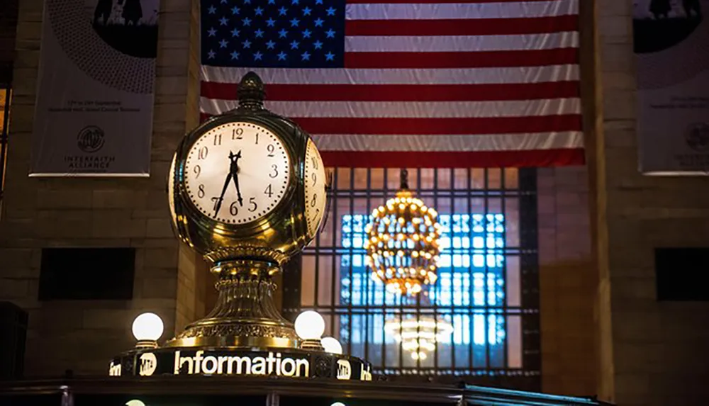 The image features the iconic information booth clock inside Grand Central Terminal with the American flag hanging in the background