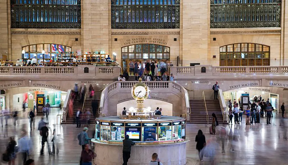 The image shows a bustling interior of Grand Central Terminal in New York City with people in motion and the iconic four-faced clock above the information booth in the center