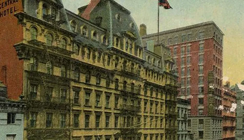 The image shows a vintage color postcard depicting a densely built urban street scene with ornate architecture from an earlier period showcasing a multi-story building with a flag proudly displayed on the facade