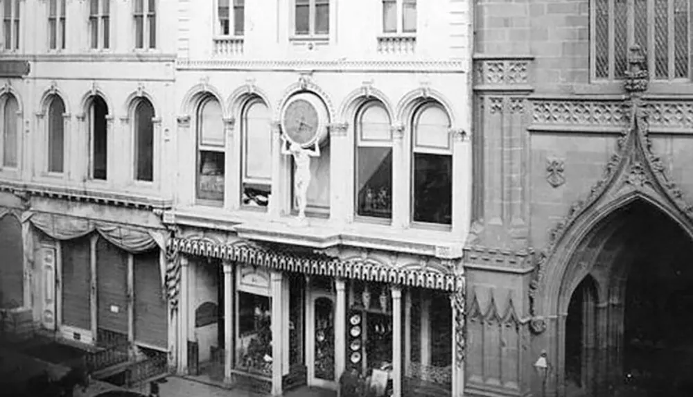 This black and white photograph shows the exterior of a European-style building with arches and decorative elements including a sculpture of a crucifix positioned above the first floor