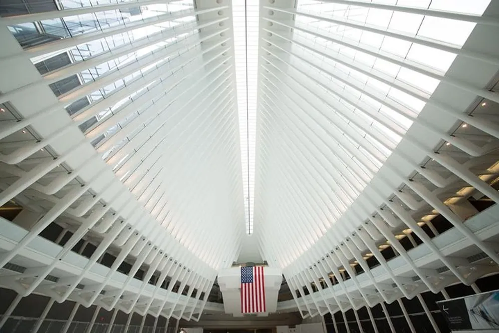 The image shows the interior of a modern building with a white ribbed ceiling structure leading the eye towards a hanging American flag