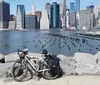 People are enjoying various outdoor activities along a riverside path with a city skyline in the background