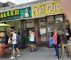 A group of people is standing in front of a store named The Pickle Guys holding pickles and smiling