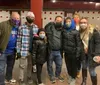 A group of people is standing in front of a store named The Pickle Guys holding pickles and smiling