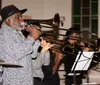 A man in a hat plays the trombone alongside other musicians in what appears to be a live jazz ensemble performance