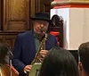 A man in a hat plays the trombone alongside other musicians in what appears to be a live jazz ensemble performance