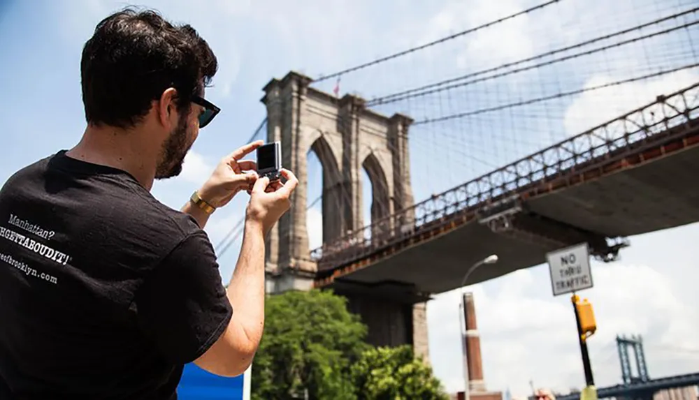 A person is taking a photograph of the Brooklyn Bridge with a small digital camera