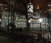 An evening view of a historic building framed by bare trees and surrounded by illuminated high-rise buildings