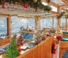 The image shows a festively decorated bar onboard a boat adorned with Christmas decorations and a view of the water outside