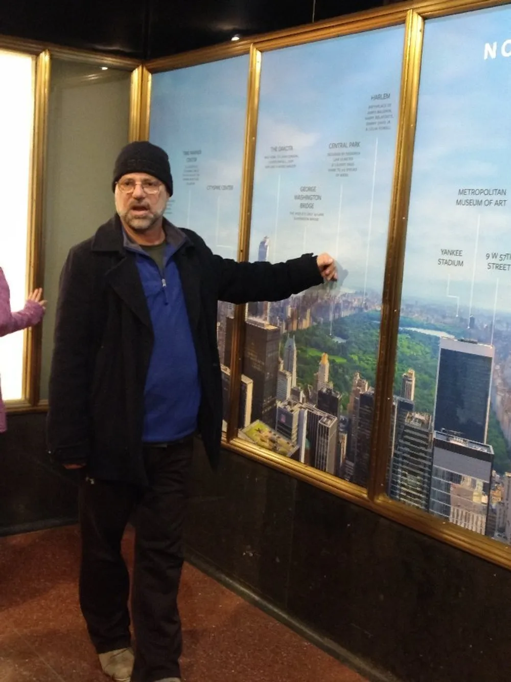 A person is posing in front of a framed aerial view map or photo of New York Citys notable landmarks