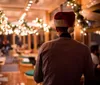 A person wearing a Santa hat is facing away from the camera overlooking a festive and warmly-lit interior adorned with holiday decorations