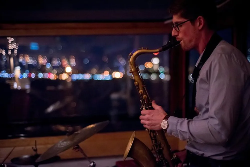 A saxophonist performs indoors at night with a backdrop of city lights through a window