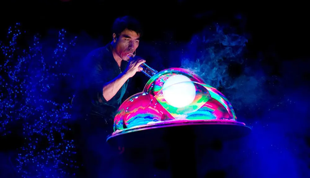 A person is creating a large colorful soap bubble on stage under dramatic lighting