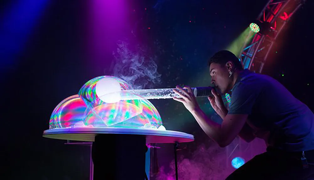 A person is blowing bubbles to create large colorful soap bubbles illuminated by stage lights in a dark setting