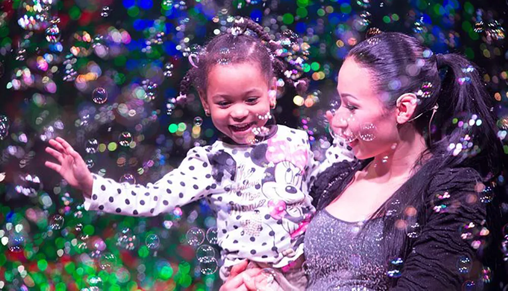 A joyful child and an adult are surrounded by a colorful swirl of bubbles sharing a moment of happiness together