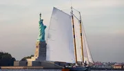 A sailboat passes by the Statue of Liberty on a clear day.