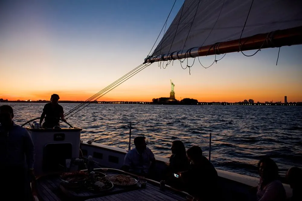 Passengers enjoy a sunset boat cruise with a view of the Statue of Liberty in the background