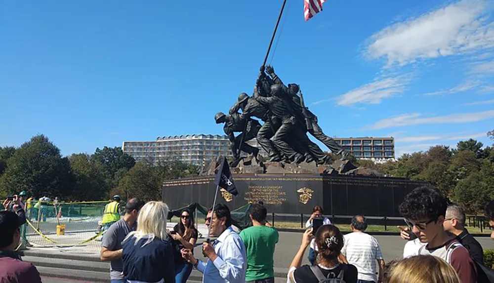 The image captures a group of visitors gathered around the Marine Corps War Memorial also known as the Iwo Jima Memorial on a sunny day