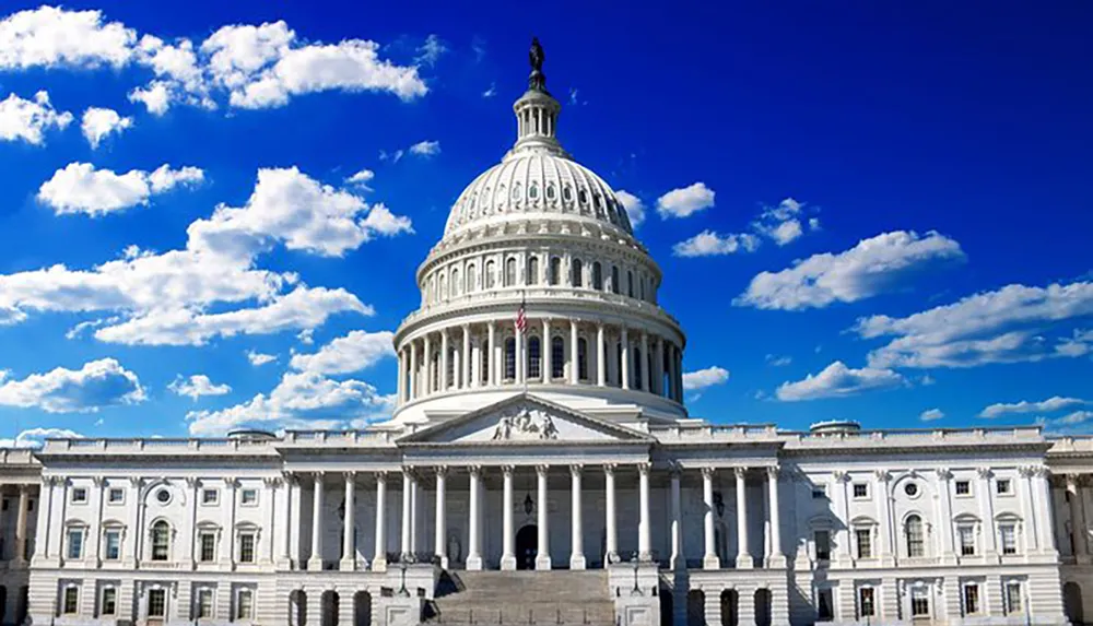 This is a frontal view of the United States Capitol Building against a backdrop of a clear blue sky scattered with fluffy white clouds