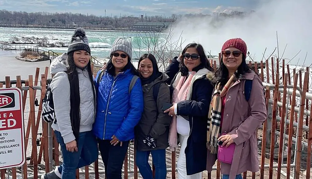 A group of five people pose for a photo with a misty backdrop that suggests the presence of a large waterfall or rapid waters possibly near a tourist attraction