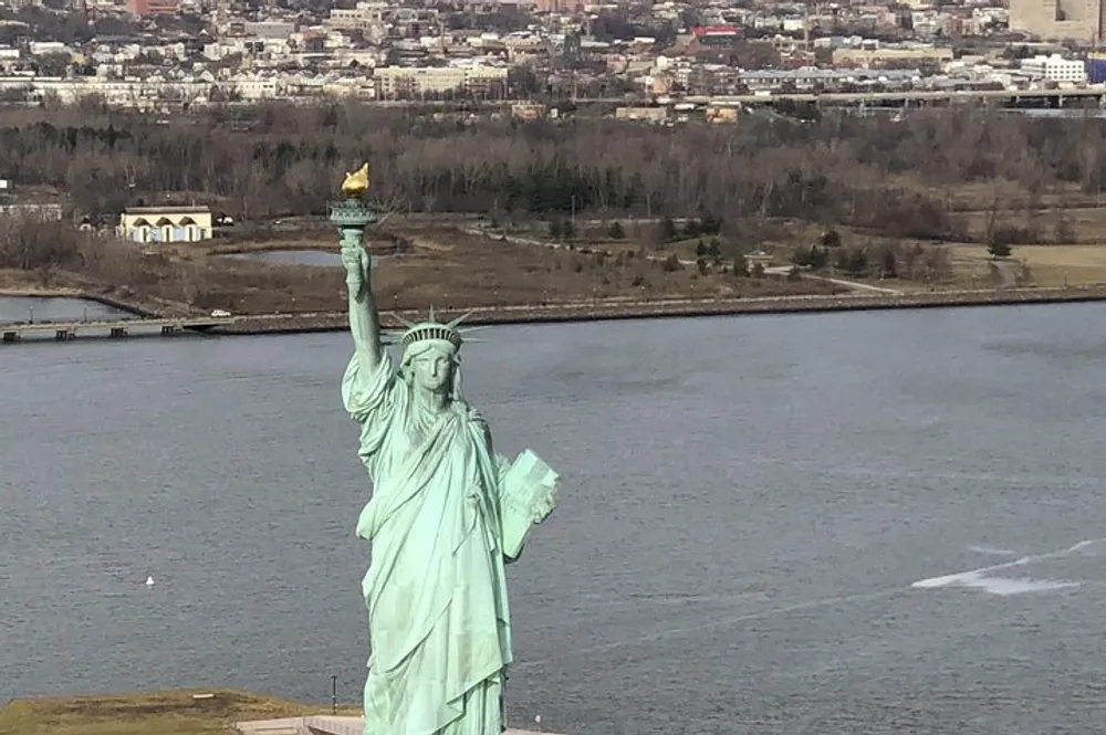 The image shows the Statue of Liberty against a backdrop of water and distant city structures