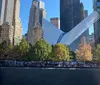 The image shows the Oculus structure at the World Trade Center site in New York City with a view of the reflecting pool of the National September 11 Memorial and surrounding skyscrapers on a clear day