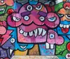 The image displays a grayscale mural on a brick wall featuring a surprised or startled looking face with elements of the wall seemingly pixelating or breaking apart on one side