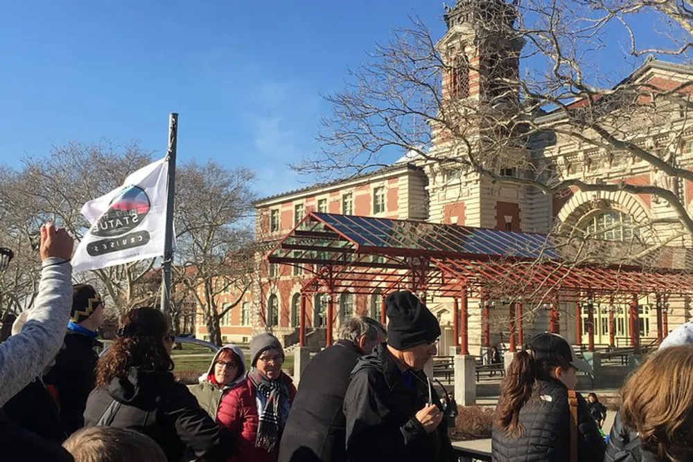 A group of people is gathered outside of a historic building possibly on a guided tour as indicated by someone holding a flag likely symbolizing the groups guide